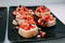 Bruschetta with fish and tomatoes on a black plate. Italian bruschetta in a cooking class