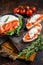 Bruschettas with stracciatella cheese, chopped cherry tomatoes and rosemary. Dark background. Top view