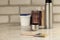 A brush lies next to a plastic paint bucket with a blue lid, a metal can, a thermos with a cup on an old white vintage wooden