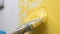 Brush slowly descends down on white wall and paints it yellow. Wall painting concept. Close-up view
