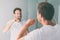 Brushing teeth man looking in mirror of home bathroom using toothbrush in morning routine for clean dental oral care