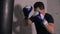 Brutal boxer in gloves punching combat bag in boxing club. Sportsman training kick with punching bag on white brick wall