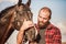 Brutal guy with a beard leads a horse. Farmer in a plaid shirt and