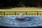 Bubbling fountain of water before open fence, green grass and dark trees, copy space