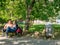 Bucharest/Romania - 05.30.2020: Garbage bin full of trash. Overflowing garbage bin and a couple sitting on bench. Environmental