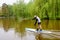 Bucharest, Romania - 1 May 2021: Man paddling on water and green weeping willow trees on the shoreline of Titan Lake in Alexandru