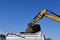 Bucket from a backhoe unloads earth into a truck box