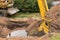 A bucket of excavator with a pile of sand and earth buries sewer concrete rings in the industrial zone