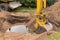 A bucket of excavator with a pile of sand and earth buries sewer concrete rings in the industrial zone