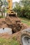 A bucket of excavator with a pile of sand and earth buries sewer concrete rings in the industrial zone