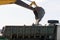 Bucket of an excavator pouring rock on the back of a truck on a sky background