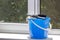 Bucket with a rag and a rubber clip for washing windows stands on a windowsill against a dirty window.