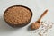 Buckwheat uncooked grains in wooden bowl on gray background close up. Wooden spoon with grits. Healthy, dietary food