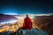 Buddhist monk sits on mountain top and looks at city and sky at night, generative AI