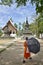 A Buddhist monk with umbrella walks towards the Wat Aham temple of Luang Prabang, Laos