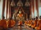 Buddhist monks in orange robes meditating in temple. Monks facing a golden Buddha statue during meditation. Concept of