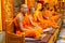 Buddhist monks sit in a temple in orange robes,