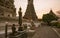 Buddhist statue standing in front of the ancient tiled Wat Arun temple, Bangkok, Thailand