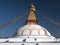 Buddhist stupa with prayers flags and a yellow lotus painted in the dome and bright blue sky.