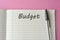 Budget planning concept. Top view of notepad with word Budget on pink minimalist background. Write idea success solution concept