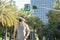 A buff asian guy walks at a beautiful city street lined with date palms. Wearing a face mask, new normal scene outdoors