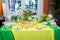 Buffet with a yellow-green tablecloth with snacks, desserts and a bouquet of tulips