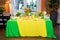 Buffet with a yellow-green tablecloth with snacks, desserts and a bouquet of tulips