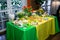 Buffet with a yellow-green tablecloth with snacks, desserts and a bouquet of tulips