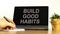 Build good habits symbol. Tablet with words `build good habits`. Businessman hand with pen, house plant. Beautiful white