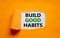 Build good habits symbol. Words `Build good habits` appearing behind torn orange paper. Beautiful orange background. Business,