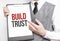 BUILD TRUST inscription on a notebook in the hands of a businessman on a gray background, a man points with a finger to the text