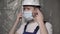 Builder in blue overalls and white hard hat puts on face mask.