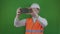 Builder or engineer takes a pictures on the smartphone of construction works. Chromakey. Boss or chief in a white helmet