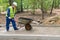 A builder in a helmet carries an empty trolley for transporting materials and she has a flat tire