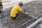 Builder in his orange gloved and yellow shirt prepares the surface before laying the paving stones with the ruler of the