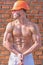 Builder with muscular torso and helmet, brick wall on background. builder concept. Builder with strong muscular