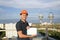 Builder in a protective helmet with a tablet for writing in his hand is standing on the roof of a building overlooking the city