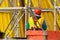 Builder in red helmet standing opposite of yellow scaffolding