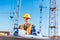 Builder in reflective vest and hardhat standing at construction site and holding