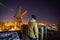 Builder on rooftop of unfinished modern building on crane and construction site background, night view