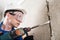 Builder in safety glasses and helmet drills a wall with a perforator, side view