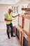 Builder Wearing Hard Hat With Clipboard Checking Delivery Of New Kitchen Units Inside Property