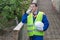 Builder in a yellow vest discusses by phone the construction time standing on the background of the stairs