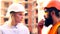 Builders communicate on the construction site. A woman in a white helmet communicates with a bearded man in an orange