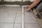 A building contractor is installing large square slip resistent tiles on a bathroom floor using a spirit level and trowel to apply