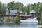 Building in a grassy area on the coast of a lake during daytime, and surrounded by trees. Yacht parked in the lakeside harbor.