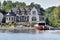 Building in a grassy area on the coast of a lake during daytime, and surrounded by trees. Yacht parked in the lakeside harbor.