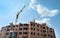 Building of a multi-storey brick house. Crane supplies construction materials to builders at a height of