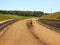 Building of new highway, scraper modify surface or gravel. Man in shorts is going.