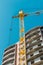 Building under construction and construction crane against blue sky and bright sun on summer day. Bottom view